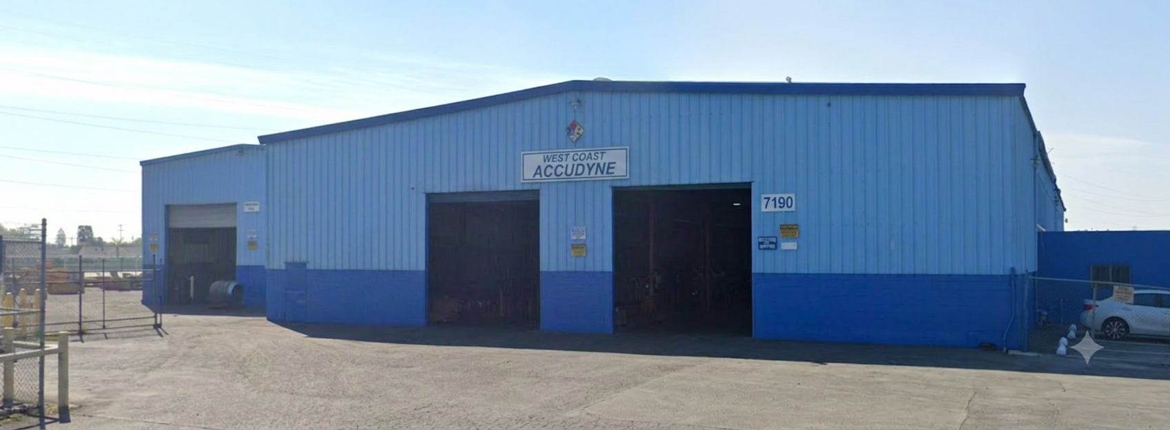 Exterior view of the West Coast Accudyne manufacturing facility, featuring the main production building with multiple large service bay doors for industrial equipment fabrication, assembly, and heavy manufacturing operations.